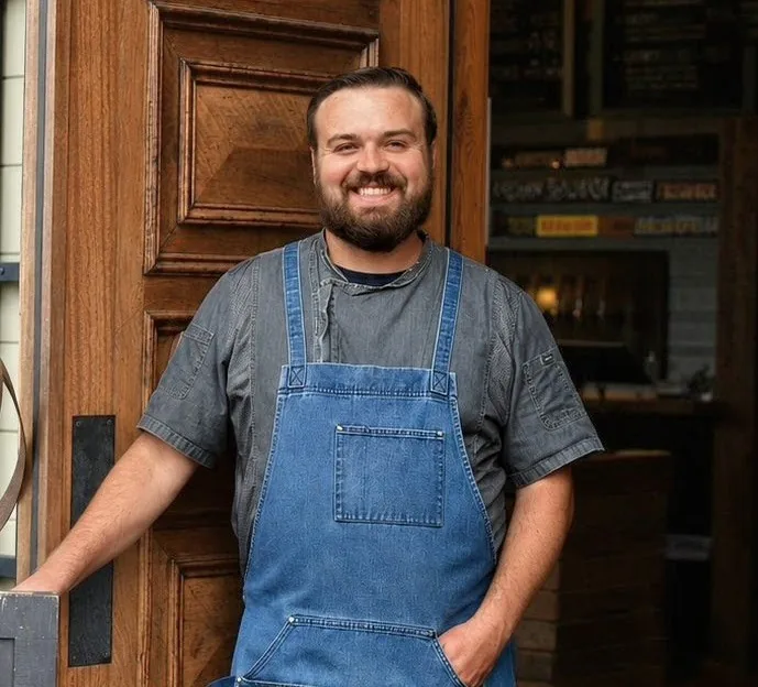 Blake Gagnon, chef and owner of Thyme to Dine, smiling in a doorway wearing a denim apron