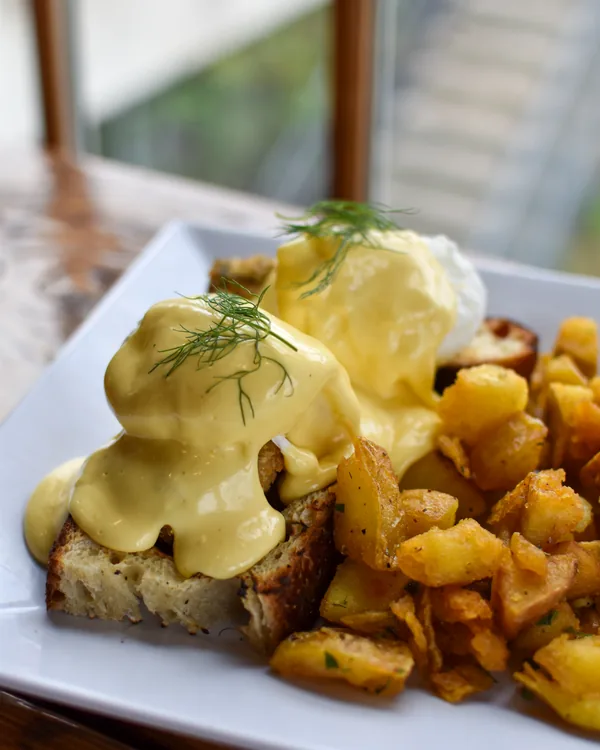 Eggs benedict with hollandaise and dill beside a pile of crisp herbed breakfast potatoes