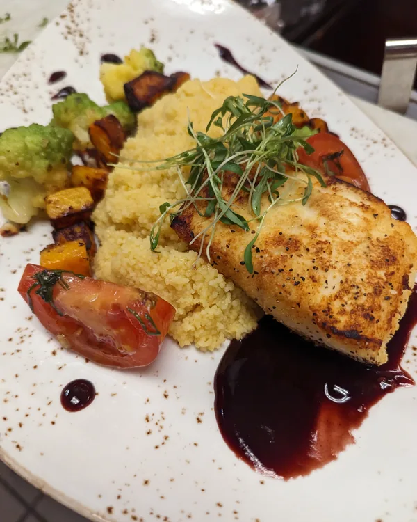 Crusted white fish with couscous, roasted vegetables and a red wine reduction on a white plate