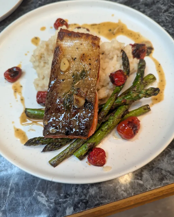Crisp-skinned salmon on parmesan risotto with charred asparagus, blistered cherry tomatoes and pan sauce