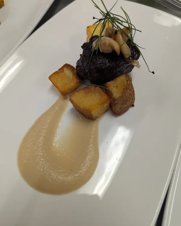 Braised short rib with roasted potatoes, confit garlic and a sweep of parsnip purée on a white plate