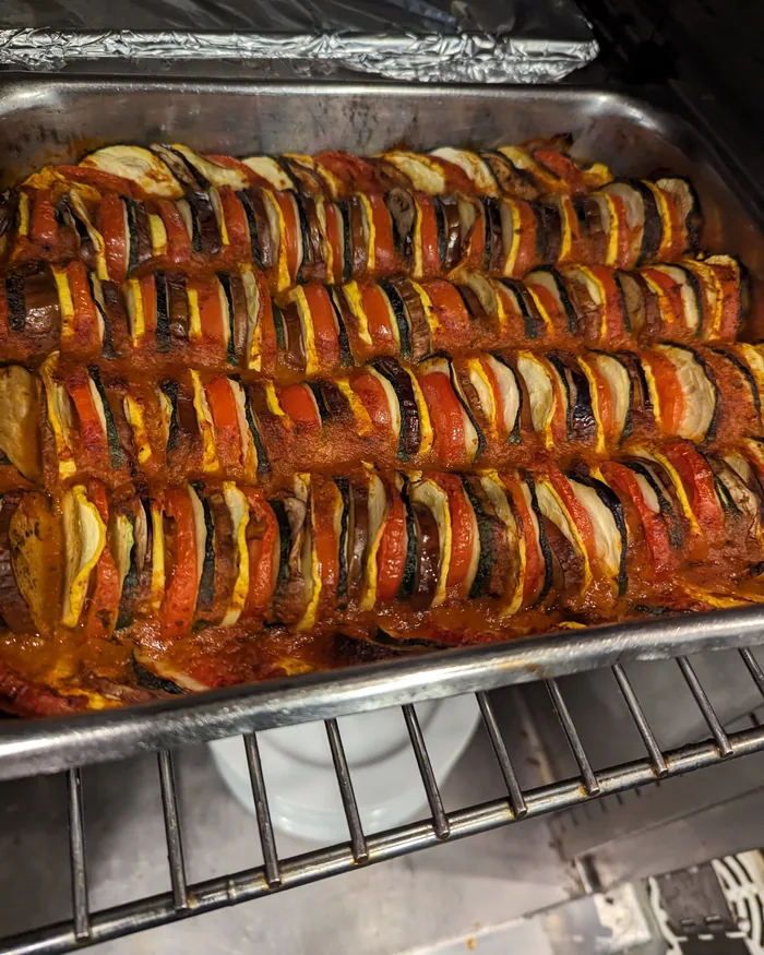 A tray of vegetable tian, rows of overlapping zucchini, squash, tomato and eggplant roasted in tomato sauce