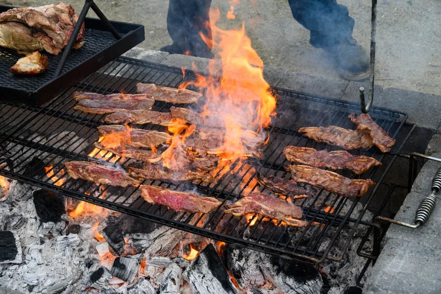Steaks laid across a steel grate with flames leaping through from the coals below