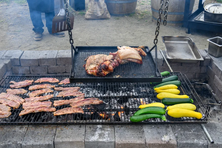 Live fire grill with pork, ribs, and yellow and green summer squash cooking over open coals