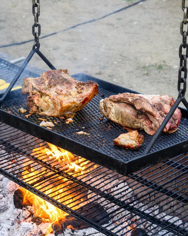 Pork cooking on a grate suspended by chains above an open fire pit