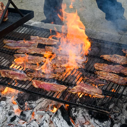 Steaks flaring over an open live-fire grill at an outdoor cook